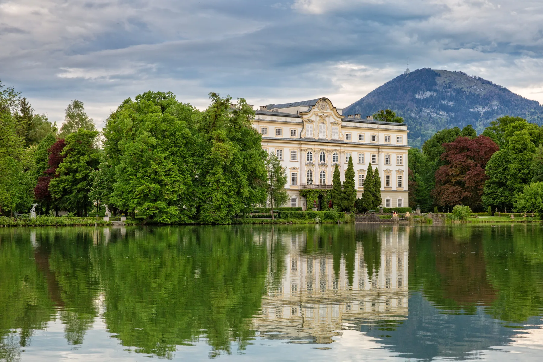 Baroque palace wedding venue on the edge of a lake near Salzburg, Austria, reflected in the water with a mountain behind