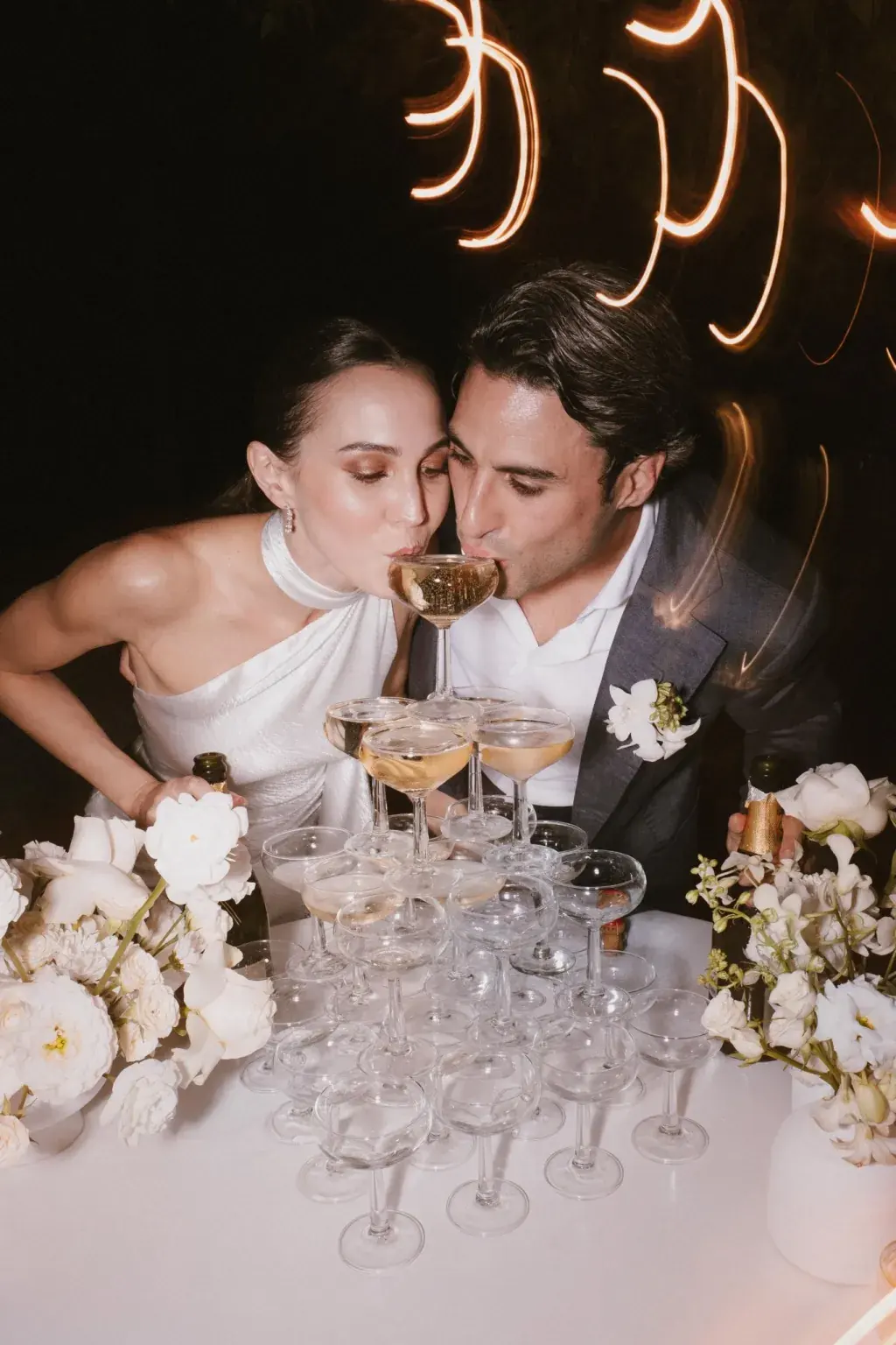Bride and groom pouring champagne into a tower of glasses at a night-time wedding reception