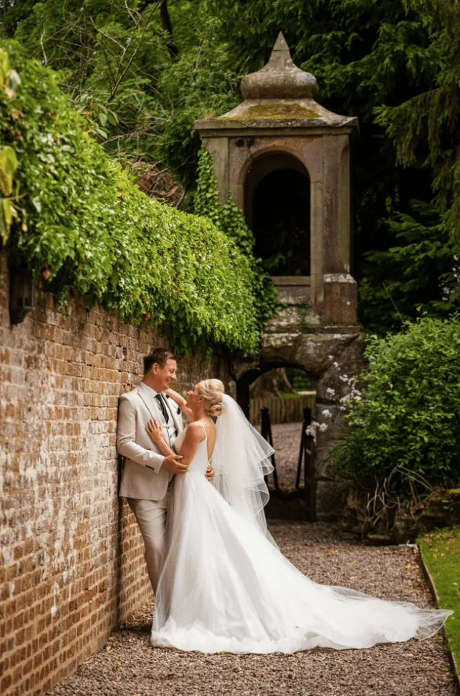 Bride and groom embracing against an ivy-covered brick garden wall at a wedding venue in Wales