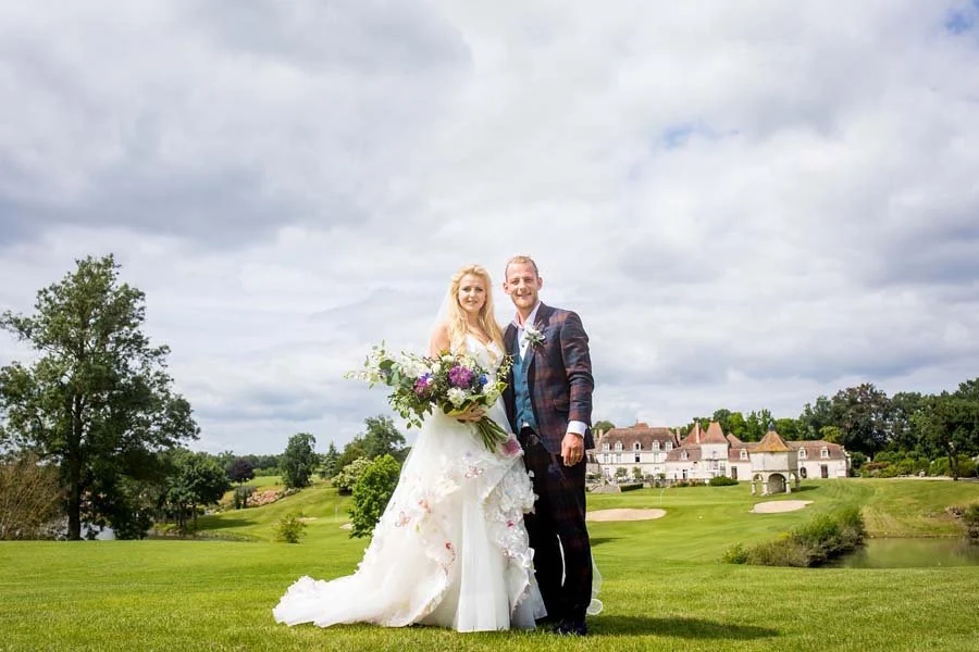 Bride and groom on the golf course with the château-style clubhouse, bunkers and lake behind them