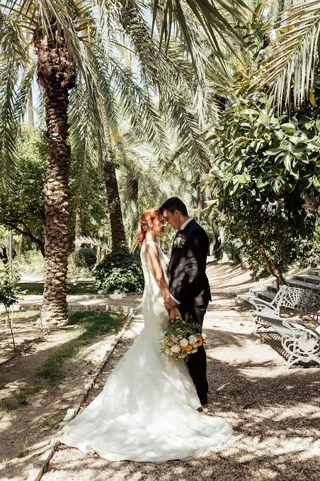 Bride and groom embracing beneath palm trees in dappled sunlight in a garden, a natural wedding portrait