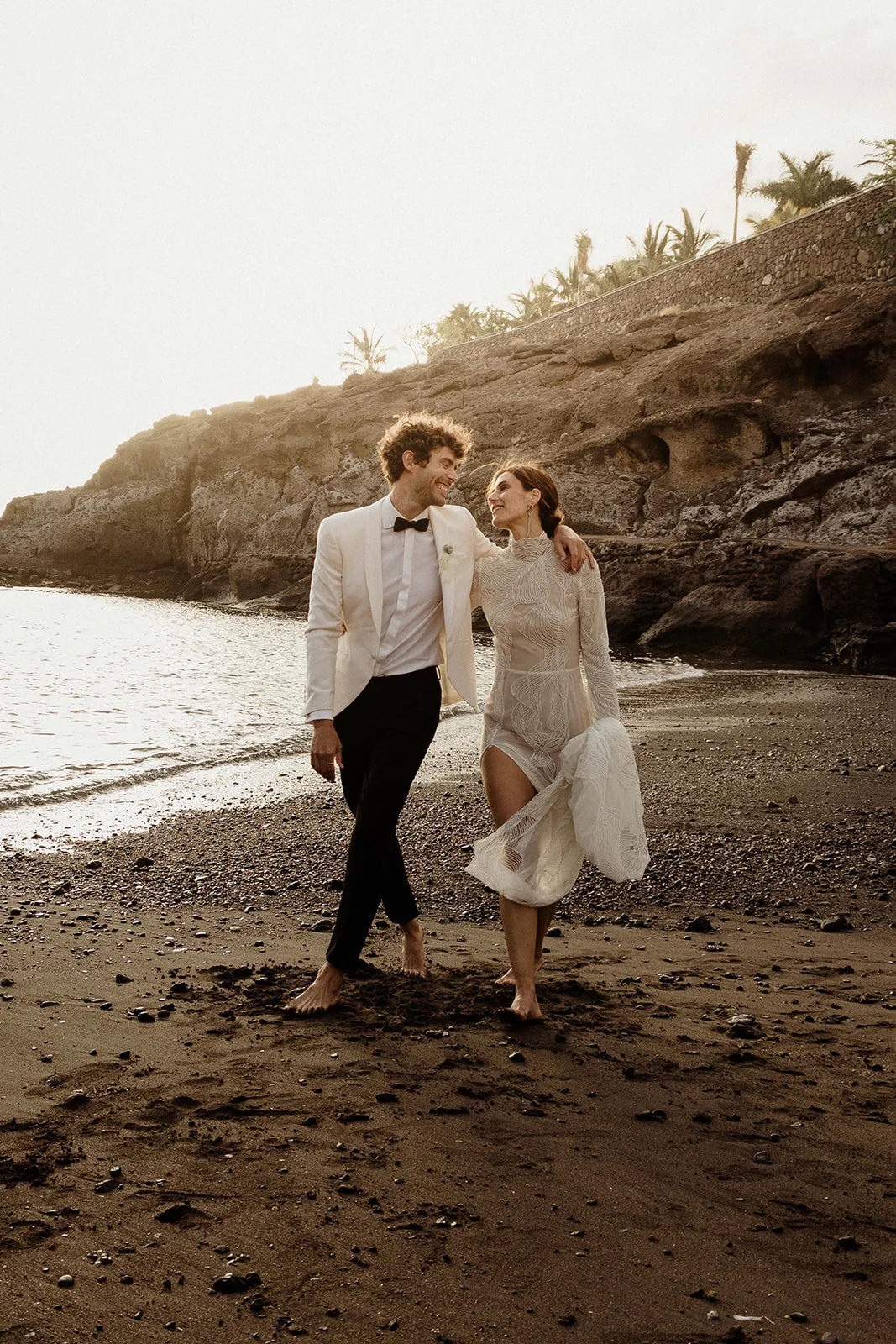 Bride and groom walking barefoot on a black volcanic sand beach in the Canary Islands
