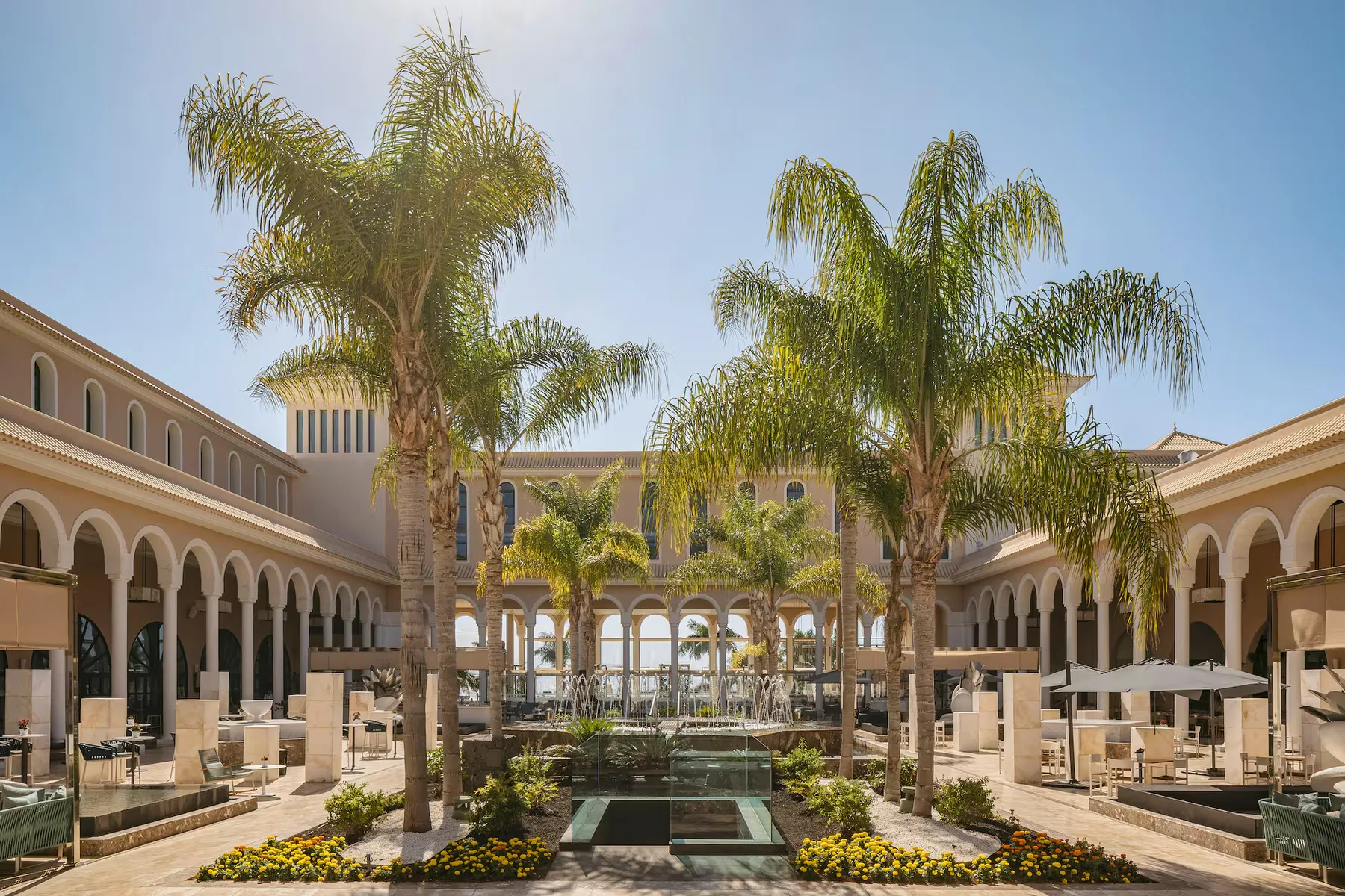 Sunlit courtyard of a luxury resort wedding venue in the Canary Islands, with tall palm trees, arched colonnades and fountains