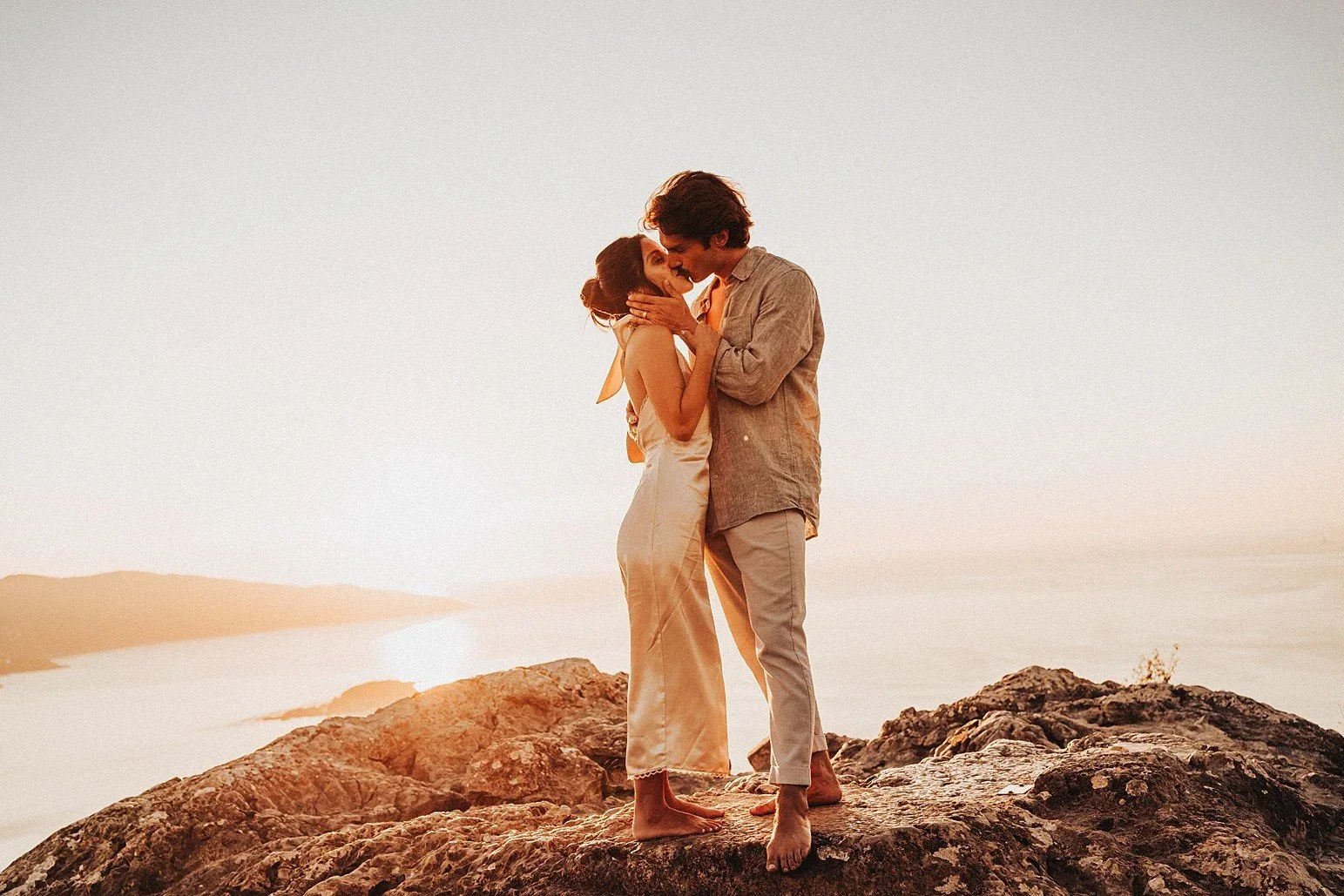 Couple kissing on a rocky clifftop above the sea in warm golden evening light