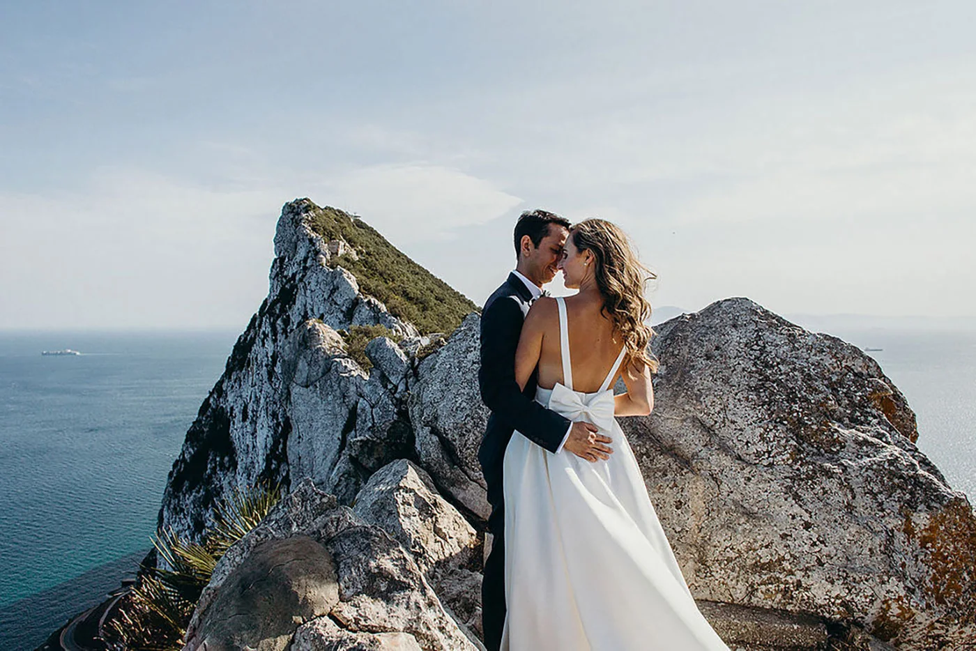 Bride and groom embracing on the summit of the Rock of Gibraltar, with the sea and the Strait behind them