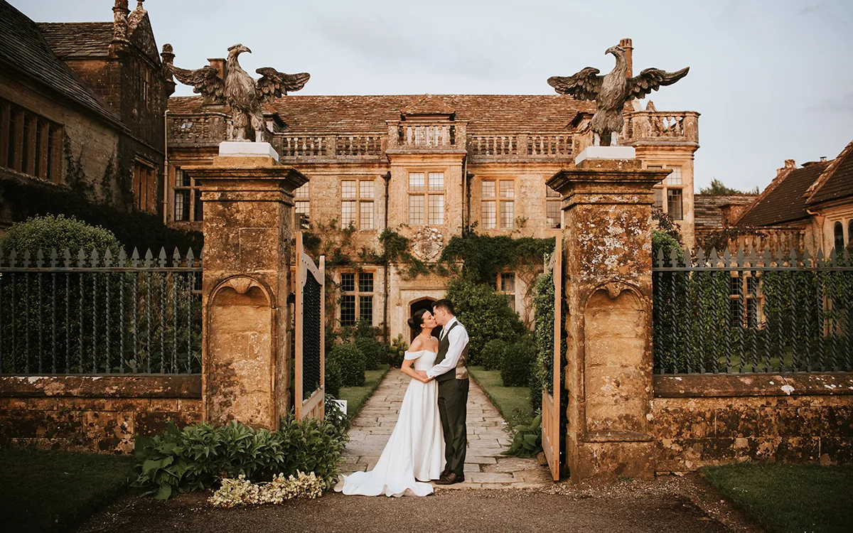 Bride and groom kissing at the stone gateway of an English manor house wedding venue