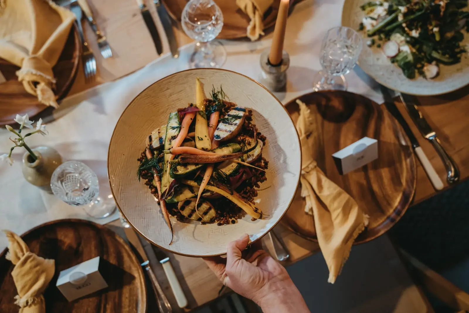 Plated wedding food of grilled courgettes, heritage carrots and grains served to a guest at a candlelit wedding table