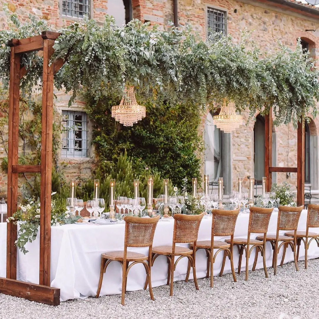 Wedding table with chandeliers, candles and greenery under a pergola at a villa