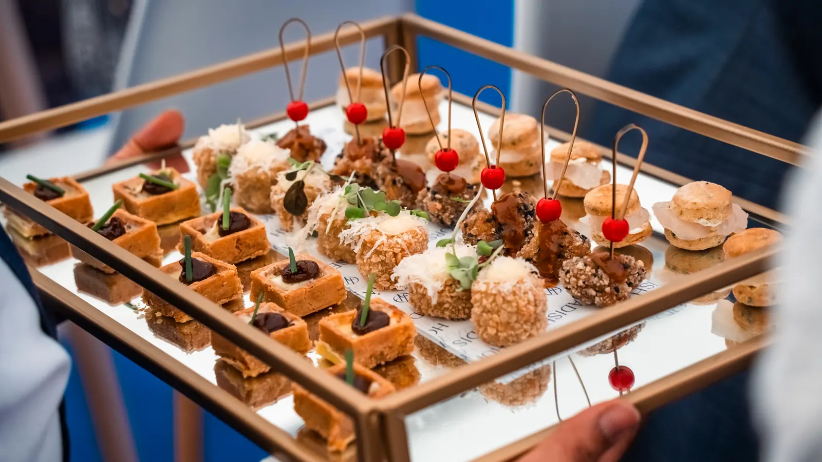 Wedding canapés of mini tartlets, croquettes and savoury macarons served on a gold and mirrored tray at a drinks reception