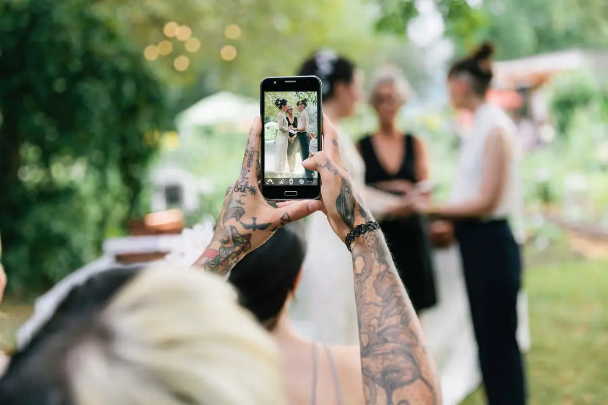 Guest filming a garden wedding ceremony on a smartphone, the kind of real-time footage a wedding content creator captures