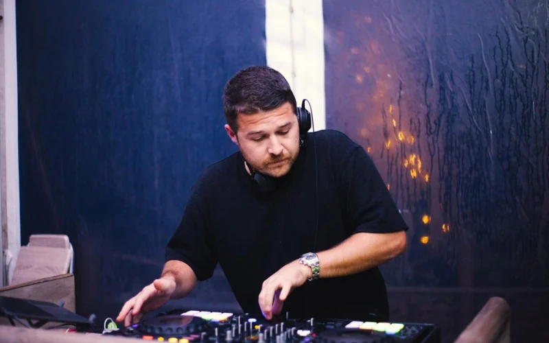 A DJ mixing at the decks during an evening wedding reception, lit in deep blue with warm lights behind