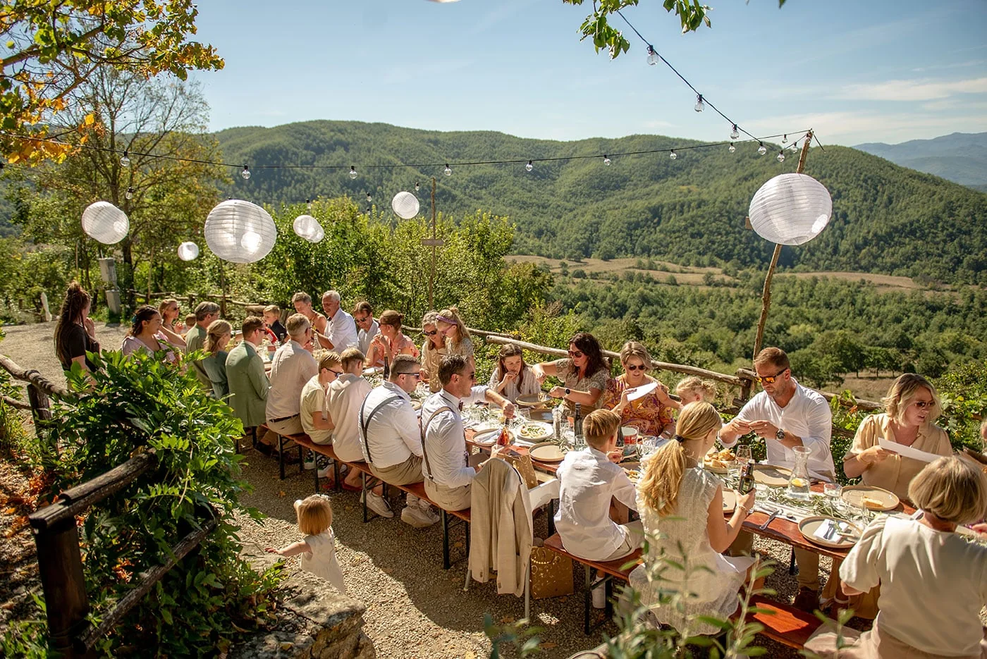 Long outdoor wedding lunch table with lanterns and flowers overlooking the hills