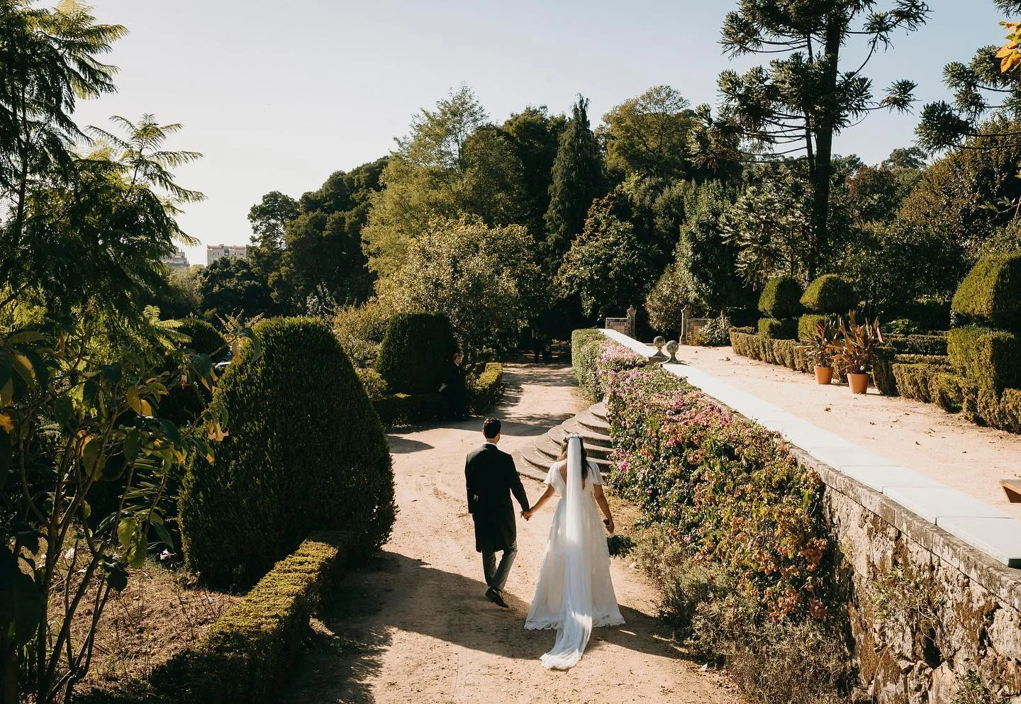 A bride and groom walking hand in hand through the formal gardens of a wedding venue in Portugal