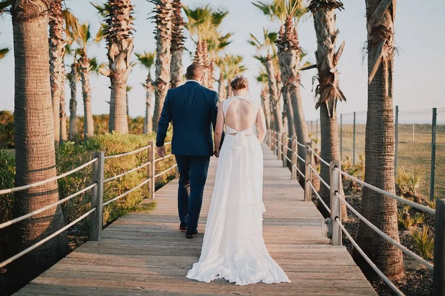 Bride and groom on a palm-lined boardwalk at sunset, a Barcelona wedding planned by Swish Soirées