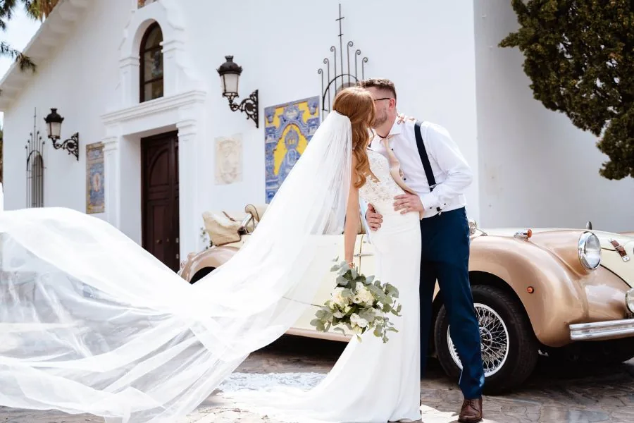 Bride and groom kissing beside a vintage car outside a church, a UK wedding planned by Swish Soirées