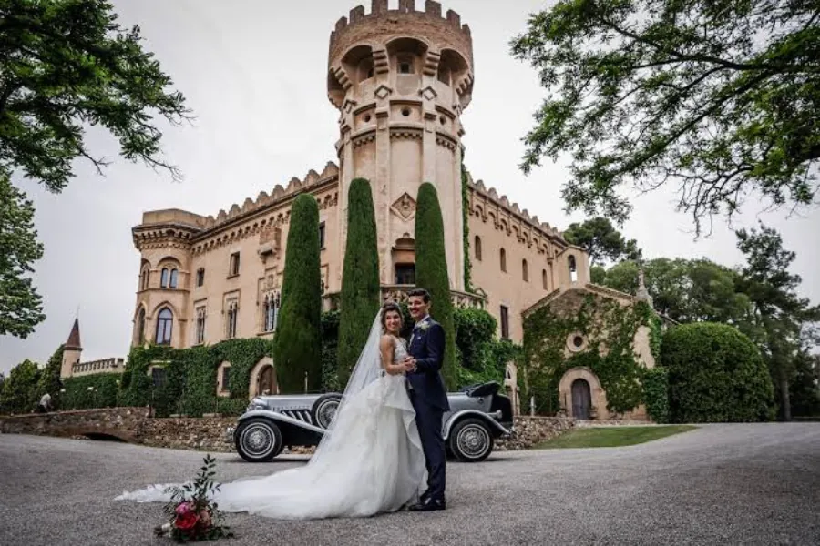 A bride and groom with a vintage car in front of Castell de Sant Marçal near Barcelona