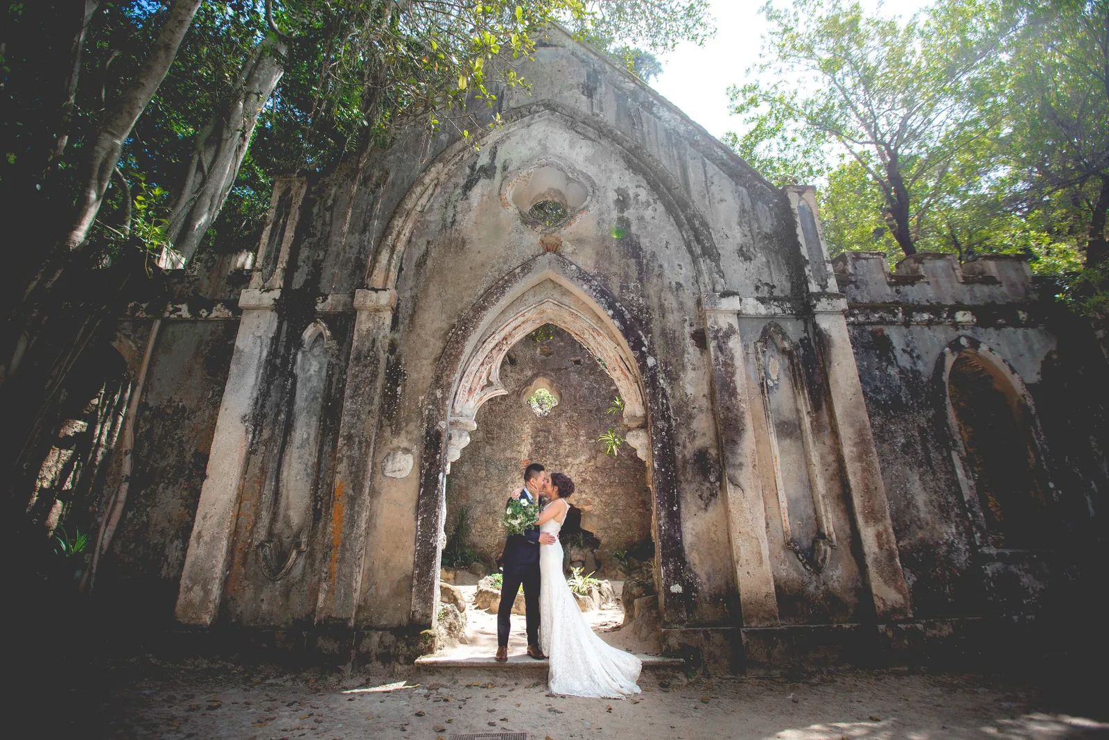 A bride and groom kissing beneath a ruined Gothic arch, a destination wedding planned by Swish Soirées